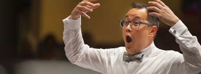 Image of a male director of a choir in mid performance.